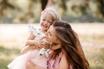 Wall Mural - Young mother is playing with her little daughter in the park on summer day. Family holiday in garden. Portrait mom with child together on nature. Mum, little daughter outdoors. Happy Mothers Day