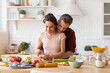 © deniskomarov - Happy wife and husband cooking romantic dinner at home kitchen. Man hugging woman from back. Couple chopping vegetable together. Fresh salad recipe preparation. Loving relationship. Family portrait