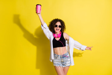 Wall Mural - Photo portrait of laughing sexy girl in sunglass earphones wearing shirt denim shorts holding paper cup isolated vibrant color background