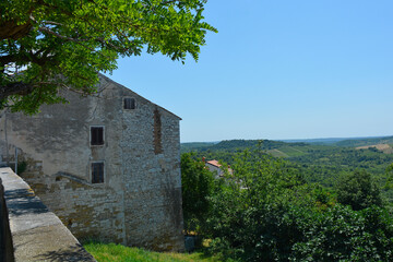 The view of the surrounding summer landscape from the historic medieval hill village of Buje in Istria, Croatia. An old village stone building is on the left
