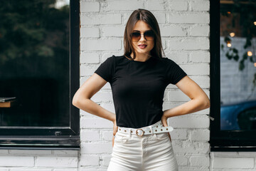 Stylish brunette girl wearing black t-shirt and glasses posing against street , urban clothing style. Street photography