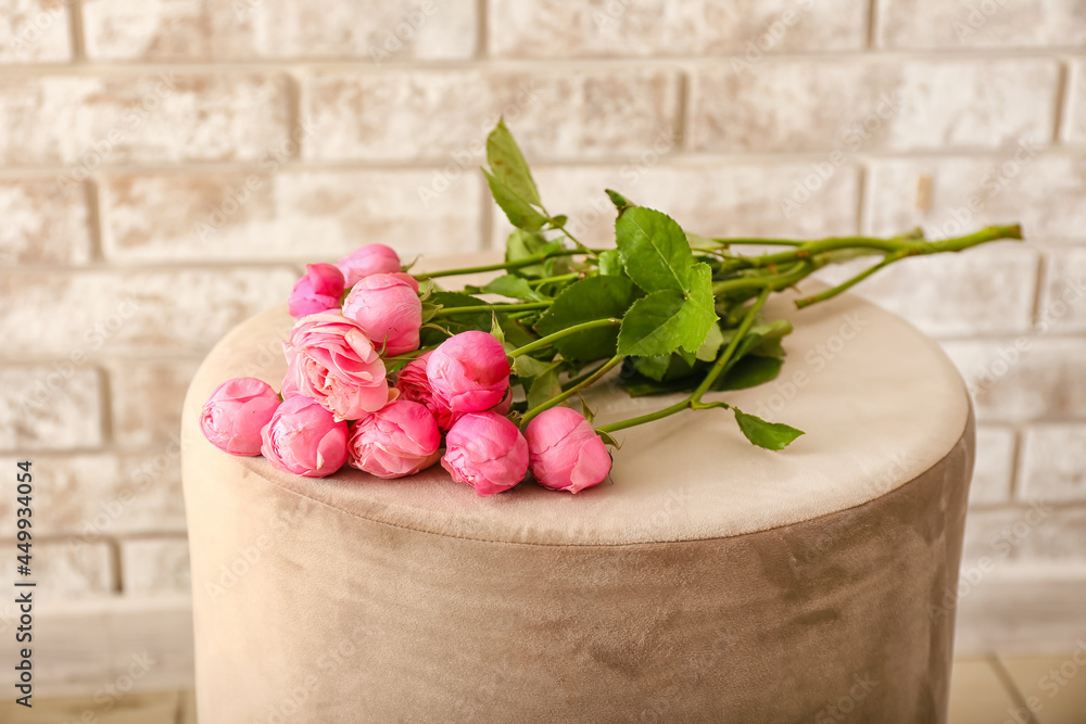 Beautiful peony roses on pouf against brick wall
