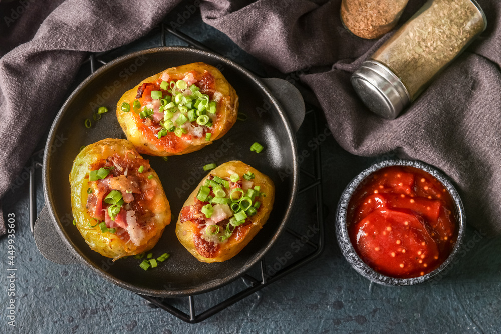 Frying pan with baked potato and sauce on dark background