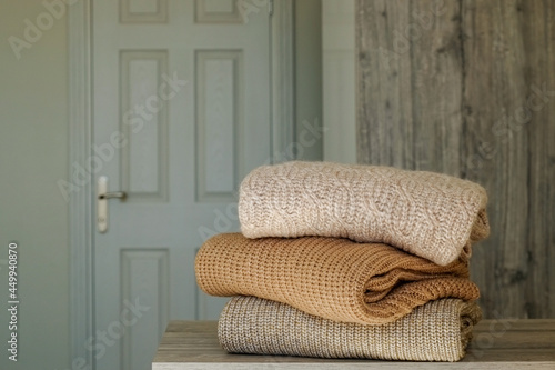 Stack of clean freshly laundered, neatly folded clothes on bedroom dresser\'s top. Pile of different sweaters of pastel colors. Copy space, close up, background.