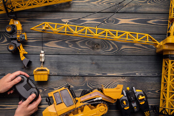 Wall Mural - Yellow construction crane toy, bulldozer and hands with a joypad on the wooden flat lay table background. Children education toys.