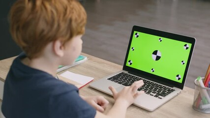 Online kids development. Little boy using online educational platform, working on laptop with green chroma key screen