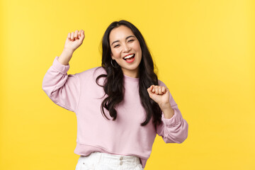 Wall Mural - People emotions, lifestyle leisure and beauty concept. Upbeat happy and cheerful asian girl dancing and having fun, partying, moving rhythm music and smiling over yellow background