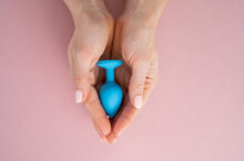 A Woman Is Holding A Blue Anal Plug On A Pink Background. Adult Toy For Alternative Sex