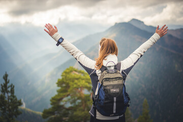 Girl with backpack enjoying sunset on peak mountain. Tourist traveler on backgroun