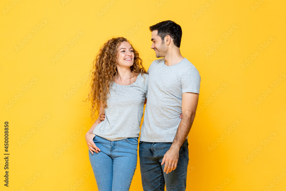Young happy interracial millennial couple holding and looking each other in the eyes in isolated yellow studio background - obrazy, fototapety, plakaty 