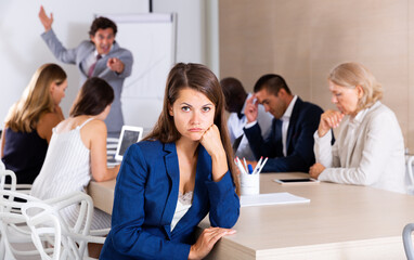 Wall Mural - Young woman sitting in meeting room looking upset because of angry boss scolding her coworkers