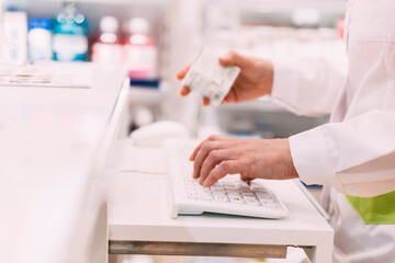 Close up of pharmacist hand holding medicine and using computer in pharmacy store