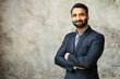 © Vadim Pastuh - Smiling middle-age Indian high skilled leader in formal suit looks at the camera, confident ambitious bearded arabic businessman stands in office with arms folded on the grey background