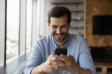 Wall Mural - happy excited male smartphone user reading, texting, smiling at screen. millennial young man using a