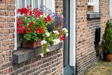 Sticker - Colorful red, white, and blue flowers in the windowsill of a small house in the historic beguinage in the Dutch city of Breda, province of North Brabant. It is a sunny day in the summer season.