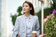 successful asian business woman walking on city street holding cup of coffee