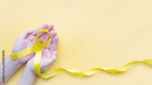 Hand holding yellow gold ribbon awareness on yellow background. Symbol for support suicide prevention, endometriosis, sarcoma bone cancer, bladder cancer, liver cancer and childhood cancer concept.
