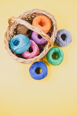 Poster - Vertical shot of colored cotton threads in a basket on a yellow background