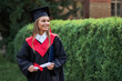 Portrait of beautiful graduate woman in graduation robe smiling and loos forward for copy space text