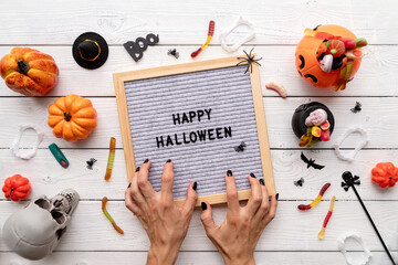 Happy Halloween words on gray letter board with candy and scary woman hands