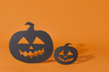 Halloween symbols, two paper pumpkins with carved faces casting shadow on orange background.