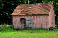 A Close Up On A Barn, Pen, Or Shelter Made Out Of Red Bricks, Tiles, And Wooden Elements Standing In The Middle Of A Well Maintained Lawn With A Small Dog House To The Side Seen On A Sunny Summer Day