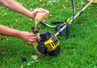 A worker pours gasoline into a trimmer or lawn mower that lies on the grass before haymaking.