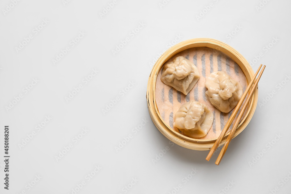 Bamboo steamer with tasty dumplings and chopsticks on light background