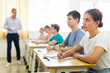 © JackF - Focused teenage girl high school student listening attentively to teacher and making notes during lesson with coursemates