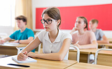 Teen Girl Listening To Lecturer And Writing In Notebook In Classroom