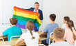 © JackF - Young progressive teacher discussing with teenage students about LGBT social movements in classroom, holding rainbow flag. Concept of supporting of LGBT or gender identity between youth..