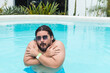 A silly chubby bearded man wearing shades shivering in the cold pool. Swimming in uncomfortably cold temperatures.