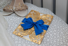 Invitation In A Golden Envelope Decorated With A Blue Ribbon Next To A Beautiful Pair Of High Heels Decorated With Lace.