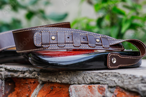 Handmade genuine leather guitar strap. Beautiful brown leather product with brass fittings. Natural old background for subject shooting.