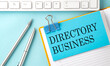 © Iryna - DIRECTORY BUSINESS text on sticker on the blue background with pen and keyboard