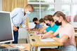 © JackF - Teenage students in protective mask studying in classroom with teacher, writing lectures in workbooks