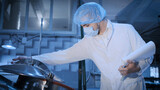 Fototapeta Desenie - A young process engineer in sterile clothing controls the brewing process of beer or other beverage in a large container in a sterile production hall.
