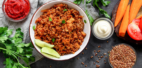 Wall Mural - Healthy food concept. Buckwheat porridge with tomato sauce. Top view. Dark background. Copy space. Diet lunch. Ingredients. Food banner.