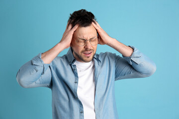 Wall Mural - Man suffering from terrible migraine on light blue background