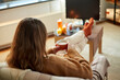 © Syda Productions - halloween, holidays and leisure concept - young woman watching tv and drinking hot chocolate with her feet on table at cozy home