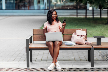 Wall Mural - technology, education and people concept - happy smiling african american student girl with laptop computer, smartphone and books in city