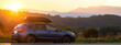 © bilanol - SUV car with roof rack luggage container for off road travelling parked at roadside at sunset.