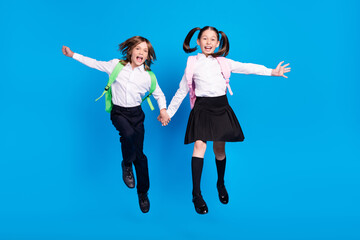 Canvas Print - Photo of astonished pretty schoolchildren wear uniform rucksacks jumping high smiling isolated blue color background