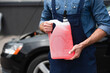 © LIGHTFIELD STUDIOS - Cropped view of repairman holding windshield washer fluid near blurred auto