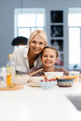 White mother and daughter smiling while having lunch in kitchen at home