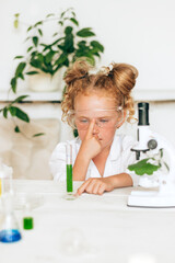 Wall Mural - Little red-haired girl in white uniform conducting chemical experiments in a laboratory.Back to school concept.Young scientists.Natural sciences.Preschool and school education of children.