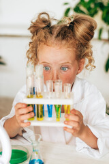 Wall Mural - Surprised little red-haired girl in white uniform conducts chemical experiments in a laboratory.Back to school concept.Young scientists.Natural sciences.Preschool and school education of children.