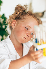 Wall Mural - Little red-haired girl in white uniform conducts chemical experiments in a laboratory.Back to school concept.Young scientists.Natural sciences.Preschool and school education of children.