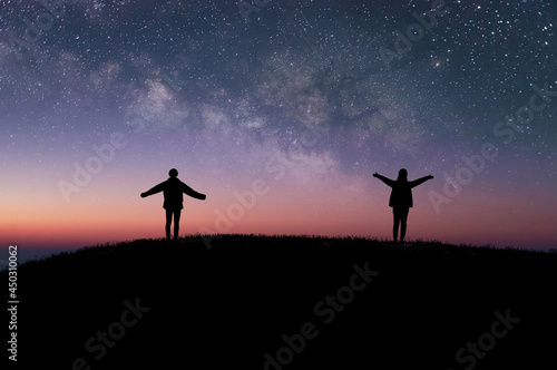 Silhouette of two tourists standing on top of the mountain and raise both hands watched beautiful night sky, star and milky way. They enjoyed traveling and was successful when he reached the summit.
