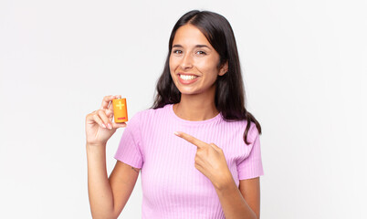 young hispanic woman smiling cheerfully, feeling happy and pointing to the side and holding batteries